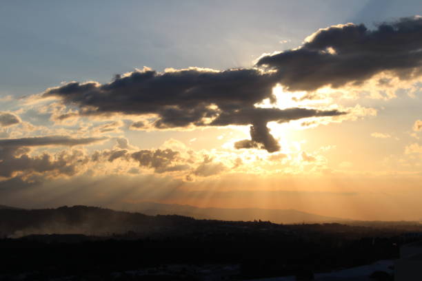 The picture shows the sun behind clouds before sunset seen from a tower in Heredia, Costa Rica
