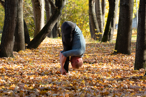 Young man doing yoga exercise in autumn park on yellow foliage