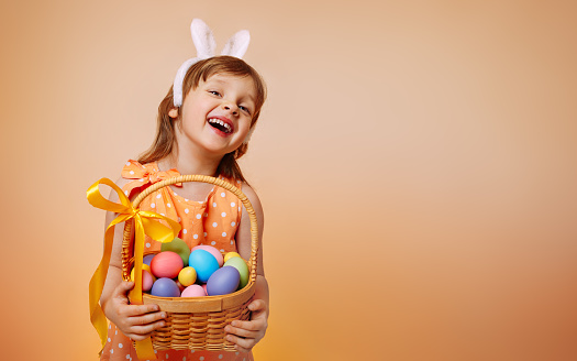 A cheerful girl with rabbit ears on her head and a protective mask with a basket of colored eggs in her hands on Easter holyday