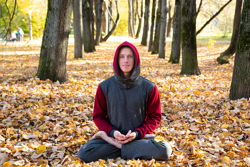 Young man doing yoga exercise in autumn park on yellow foliage