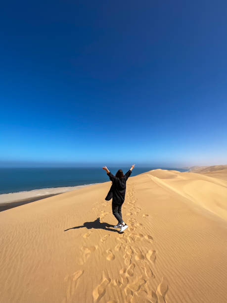 istock A young woman walks along sandy dunes on seashore. Sandwich Harbour in Namibia 1368455088