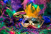 istock LV Mardi Gras sequined mask, decorated with feathers on a bed of feathered Mardi Gras feather Boas.  Colorful beads and spot lights of color. 1368457124