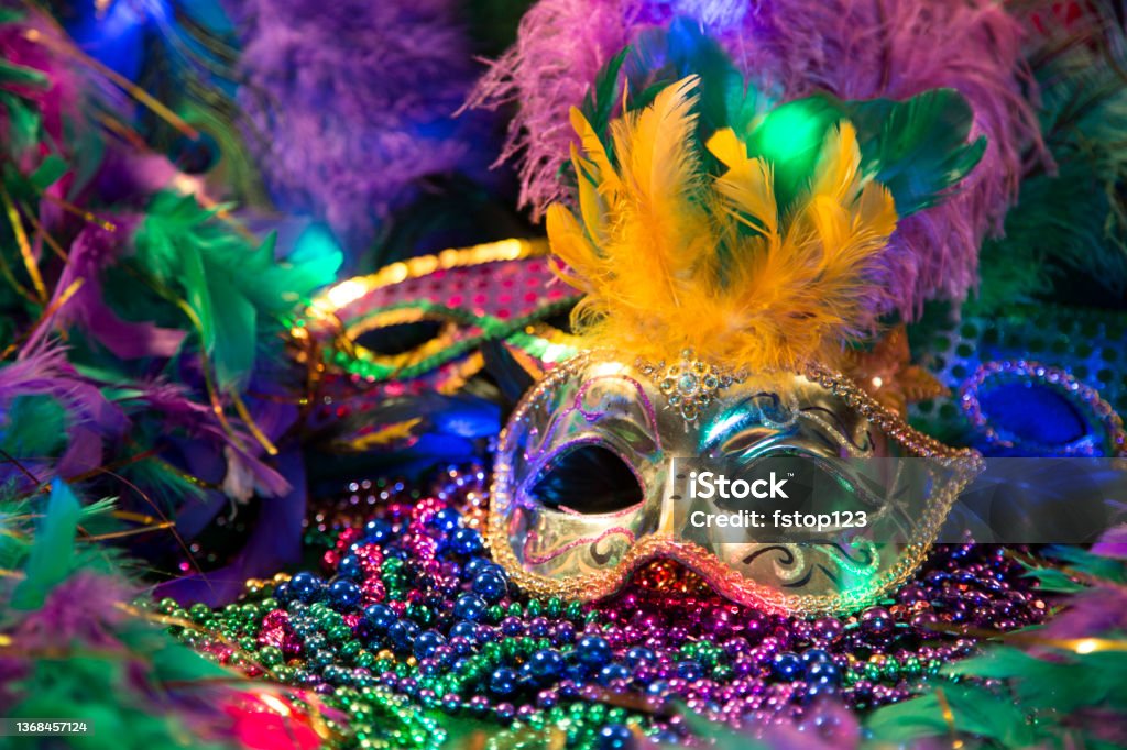 LV Mardi Gras sequined mask, decorated with feathers on a bed of feathered Mardi Gras feather Boas.  Colorful beads and spot lights of color. Mardi Gras Stock Photo