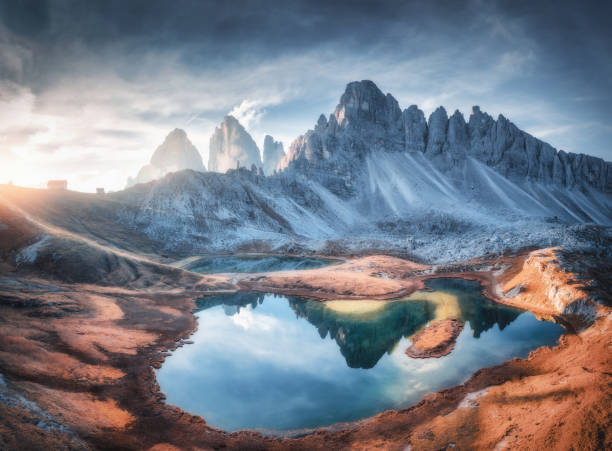 vista aérea de belas rochas, lago de montanha, reflexo na água e casas na colina ao pôr do sol. paisagem de verão com montanhas, céu azul e luz solar. dolomitas, itália. vista superior dos alpes italianos - tre cime - fotografias e filmes do acervo