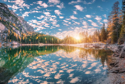 Beautiful Braies lake at sunset in autumn in Dolomites, Italy. Landscape with mountains, blue sky with clouds, water with reflection, stones, trees with colorful leaves. Lake in fall. Panorama
