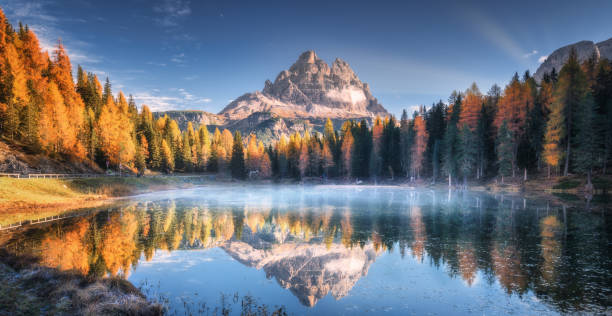 lago com reflexão das montanhas no nascer do sol no outono em dolomites, italy. ajardine com lago antorno, névoa azul sobre a água, árvores com folhas alaranjadas e rochas elevadas na queda. floresta colorida - tre cime - fotografias e filmes do acervo