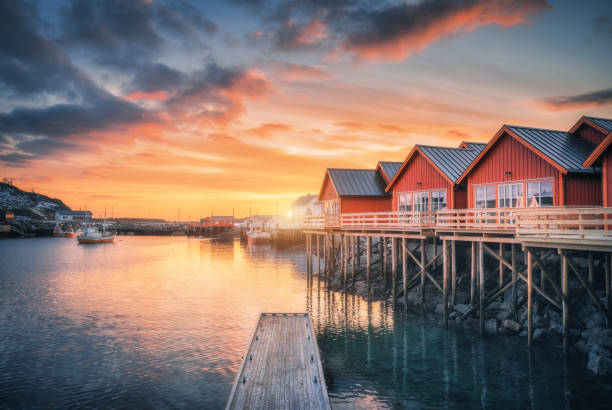 Red rorbu on wooden piles on sea coast, small jetty, colorful orange sky at sunrise in winter. Lofoten islands, Norway. Traditional norwegian rorbuer, reflection in water, boats in fishing village Red rorbu on wooden piles on sea coast, small jetty, colorful orange sky at sunrise in winter. Lofoten islands, Norway. Traditional norwegian rorbuer, reflection in water, boats in fishing village lofoten stock pictures, royalty-free photos & images