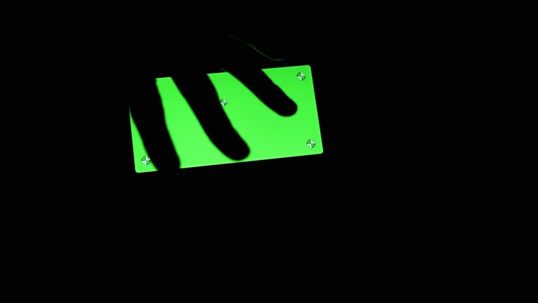 Silhouette of a Black Hand Touches a Smart Phone with a Green Screen in a Dark