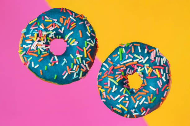 istock Two sweet doughnuts with sprinkles close-up on bright pink yellow background. Concept is fast food, happiness, good mood 1368467287