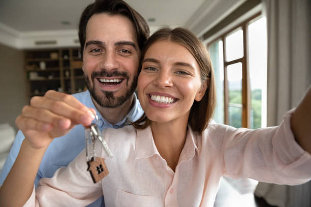 Happy couple of homeowners beginning living together Happy couple of homeowners beginning living together, showing keys at camera, taking selfie in new apartment. Excited just moved married renters, tenants self portrait. Real estate buying concept reduction looking at camera finance business stock pictures, royalty-free photos & images