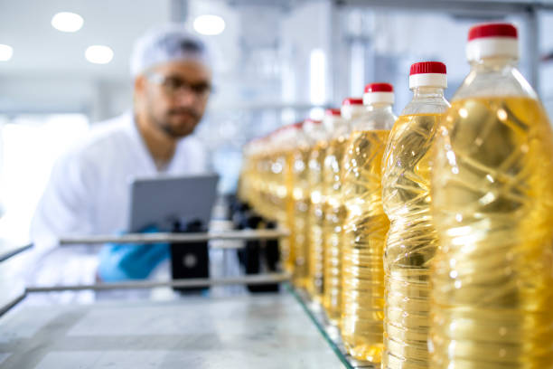 食品工場での植物油生産の瓶詰めと、ヘアネット制御プロセスを施した白衣の作業員。 - ヒマワリ種子油 ストックフォトと画像