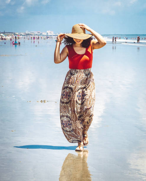 Happy stylish woman enjoying a beach holiday in a flowing skirt with sunhat Beautiful carefree Afro-Caribbean woman on a beach in Florida cocoa beach stock pictures, royalty-free photos & images