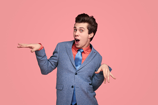 Delighted comic male entrepreneur in suit expressing happiness while looking at camera with opened mouth on pink background
