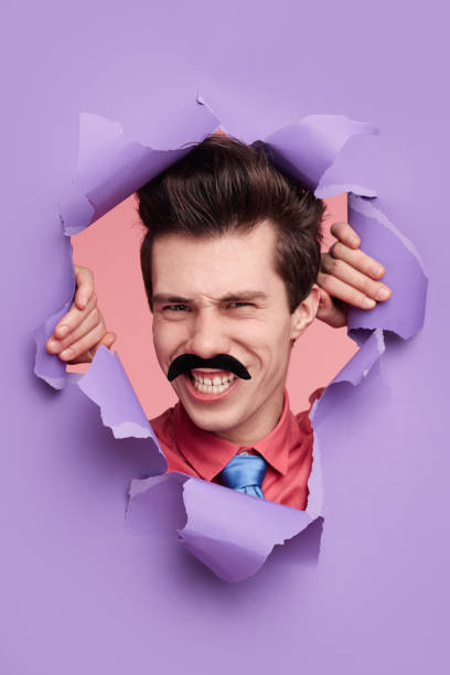 istock Funny man looking at camera through torn paper in studio 1368491544