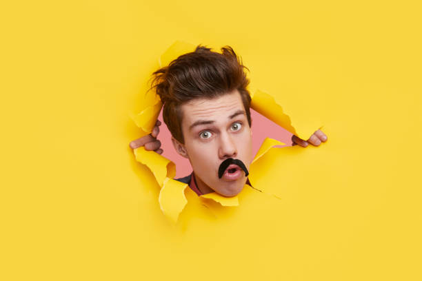 istock Funny man looking through hole in torn paper 1368491548