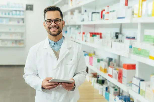 Portrait of a handsome pharmacist working in a pharmacy while checking medications on the shelf
