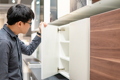 Asian man opening wooden cabinet door in furniture store choosing material to buy for house decoration. Home improvement concept
