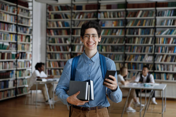 istock Excited college guy in eyeglasses using mobile phone in library 1368496832