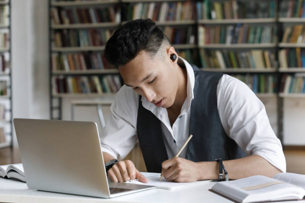 fokus pria mahasiswa asia yang serius dengan earphone nirkabel menulis catatan - high school potret stok, foto, & gambar bebas royalti