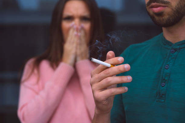 fumo passivo. uomo che fuma sigaretta vicino alla donna che si copre il viso dal fumo di sigaretta. - brutta abitudine foto e immagini stock
