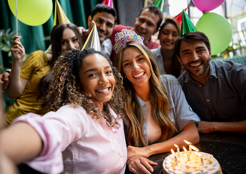 Happy group of friends taking a selfie at a birthday party and looking at the camera smiling