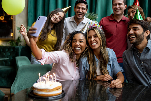 Happy multiracial group of friends taking a selfie at a birthday party using a cell phone and smiling