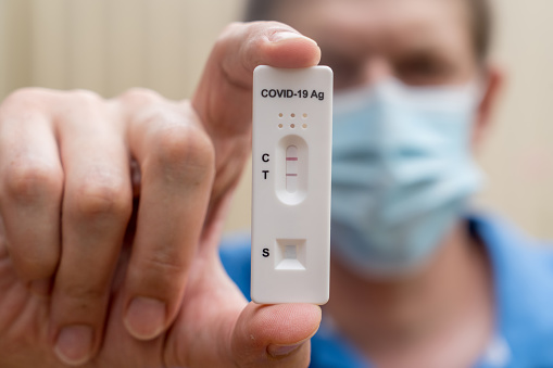 Hombre con mascarilla que sostiene un cassette de prueba rápida de antígeno Covid-19 con resultado positivo de la prueba de diagnóstico rápido. Kit de autoprueba photo