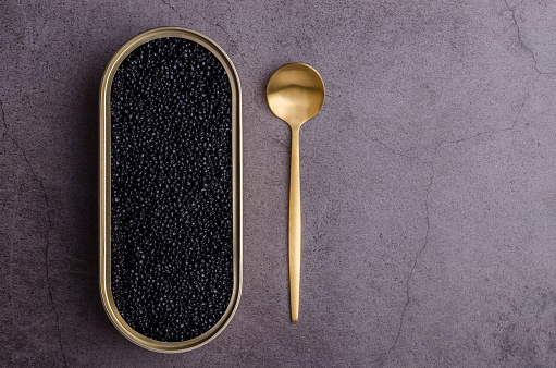 Salted black caviar in a tin can on a dark stone background. Copy space. Top view.Salted black caviar in a metal spoon on a dark stone background. Copy space. Top view.