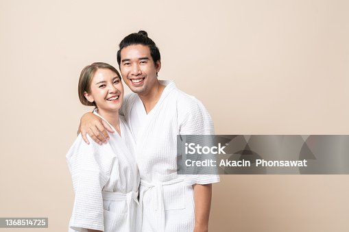 istock Asian couple in bathrobe happy smile together on brown isolated background. 1368514725