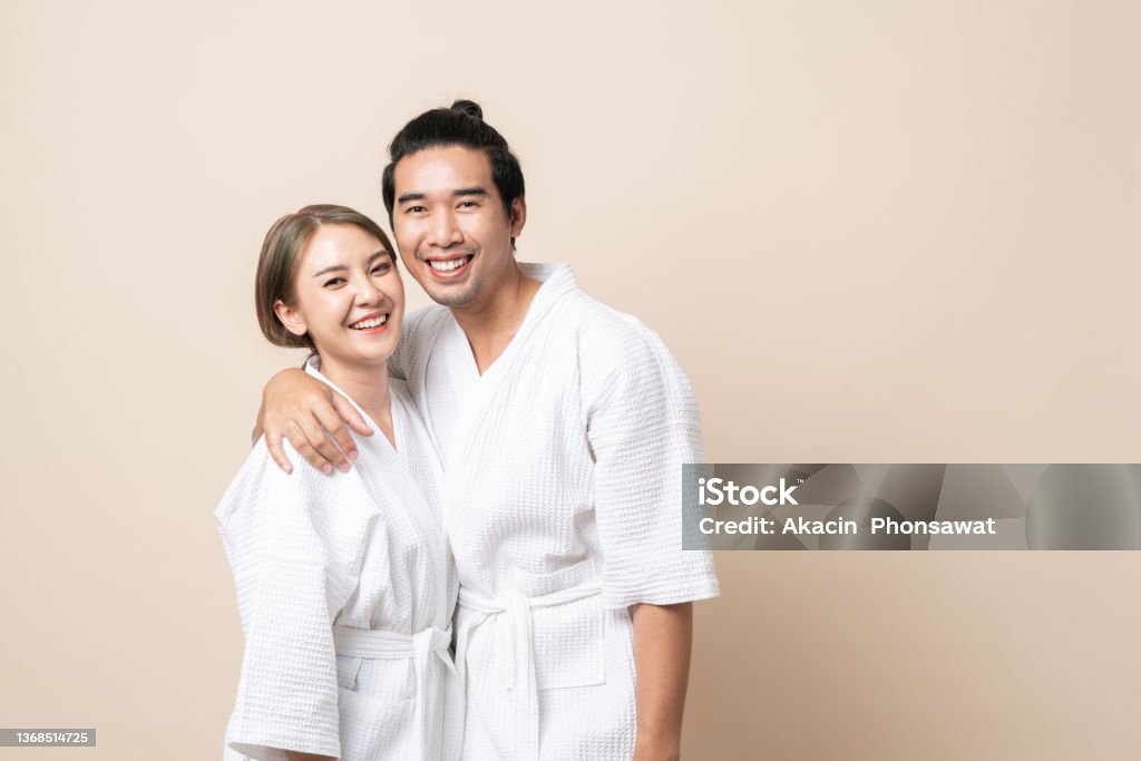 Asian couple in bathrobe happy smile together on brown isolated background. Asian couple in bathrobe or spa suit smile happy together on brown isolated studio background. Couple - Relationship Stock Photo