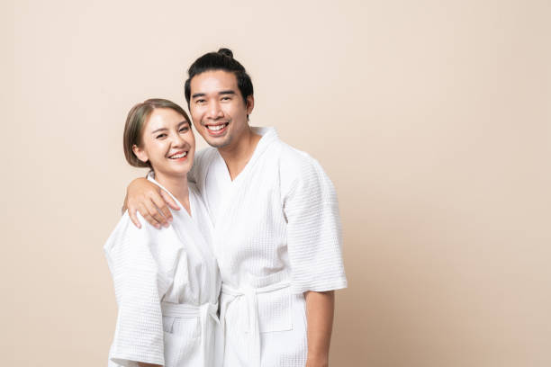 azjatycka para w szlafroku uśmiecha się razem na brązowym, odizolowanym tle. - bathrobe health spa spa treatment couple zdjęcia i obrazy z banku zdjęć