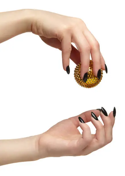 Female hand with black nails manicure and golden spiked massage ball in fingers. Isolated on white background.