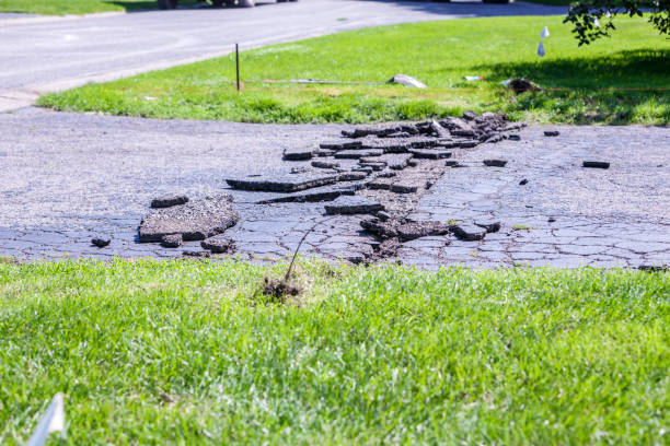 A construction team has begun breaking, digging up and removing the cracked rubble surface of an old driveway in preparation for building and paving a new asphalt suburban residential district home blacktop driveway. The first step in this image is to dig up, protect and re-route the invisible fence pet dog containment system electric wire running under the old driveway.