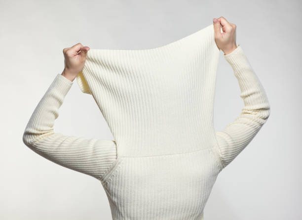 Female with hands on sweater collar hide face. Woman dressed in large white woolen sweater on gray background. Female with hands on sweater collar hide face. vogue cover stock pictures, royalty-free photos & images