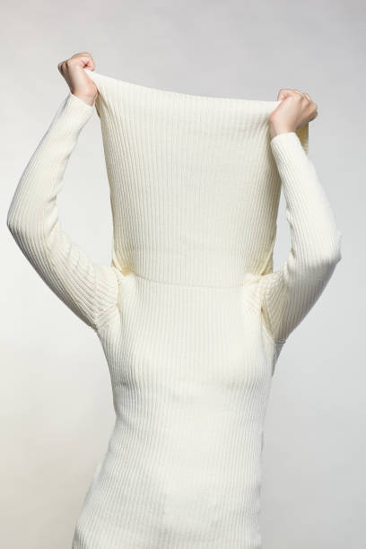 Female with hands on sweater collar hide face. Woman dressed in large white woolen sweater on gray background. Female with hands on sweater collar hide face. vogue cover stock pictures, royalty-free photos & images