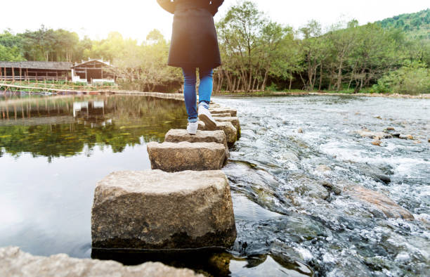 istock Woman crossing a river on stepping stones 1368525708