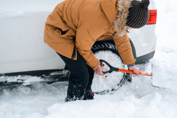 A man digs out a stalled car in the snow with a car shovel. Transport in winter got stuck in a snowdrift after a snowfall, sat on the bottom. First aid, tow truck, winter tires spikes and all-season stock photo