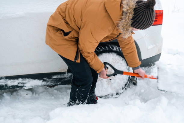 um homem desenterrou um carro parado na neve com uma pá de carro. o transporte no inverno ficou preso em uma neve depois de uma queda de neve, sentou-se no fundo. primeiros socorros, reboque, pneus de inverno e toda a temporada - off road vehicle 4x4 snow driving - fotografias e filmes do acervo