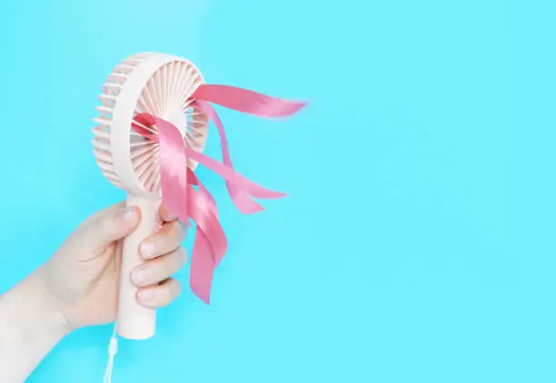 Photo of Female hand holding a pink mini fan on blue background close-up.