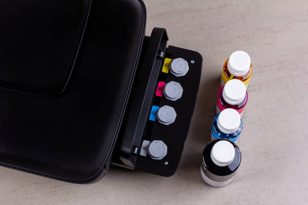inkjet four-color printer with continuous ink supply and ink bottles for refilling on grey background close-up top view