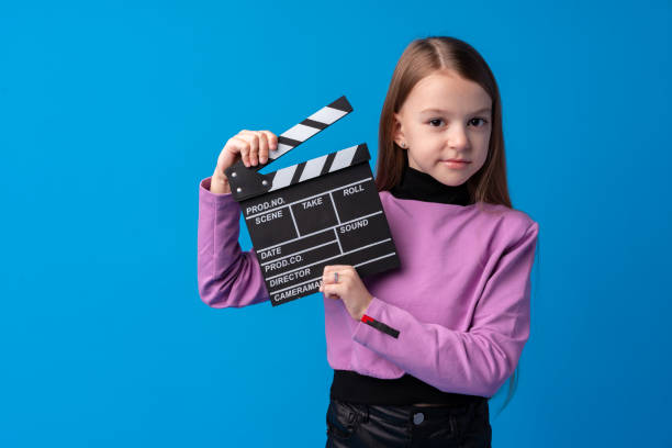 istock Smiling girl holding clapper board against blue background 1368530888