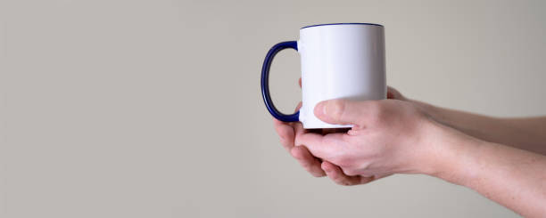 istock White mug in the hands of a man on a light background. 1368531402