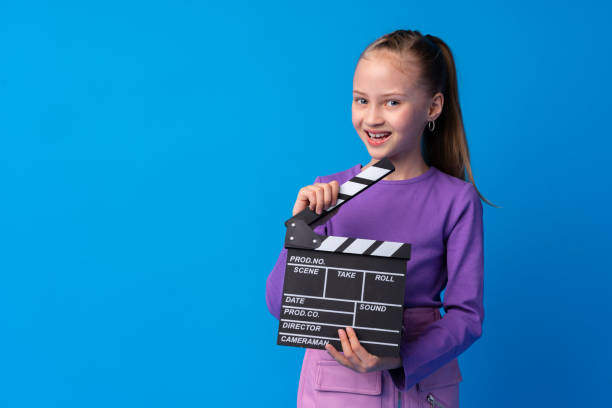 istock Smiling girl holding clapper board against blue background 1368531458