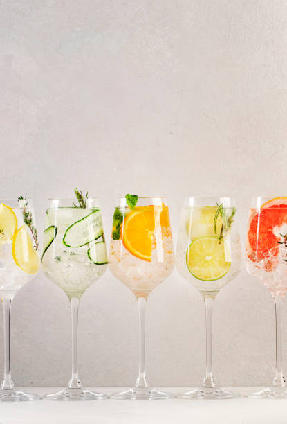 istock Gin and tonic cocktails set. Trendy Alcoholic drinks with lime, lemon, grapefruit, orange, cucumber, soda and spicy herbs in wine glasses, gray background. Summer cocktail party 1368531723