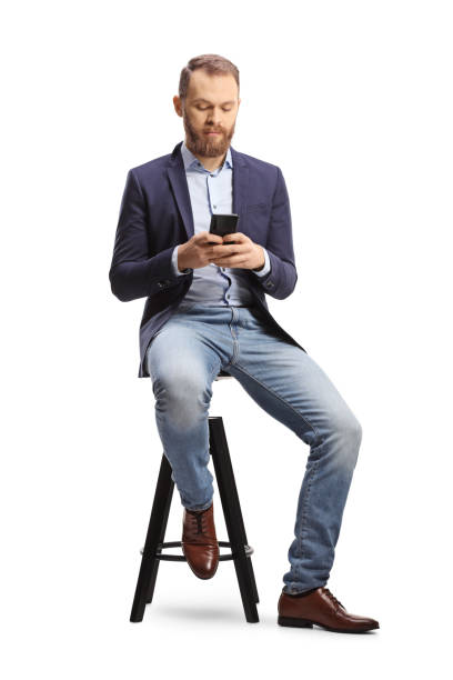 istock Bearded guy in suit and jeans using a mobile phone and sitting on a bar chair 1368533565