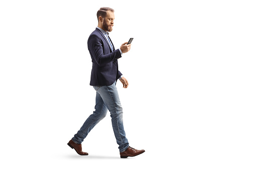 Full length profile shot of a man in suit and jeans using a mobile phone and walking
