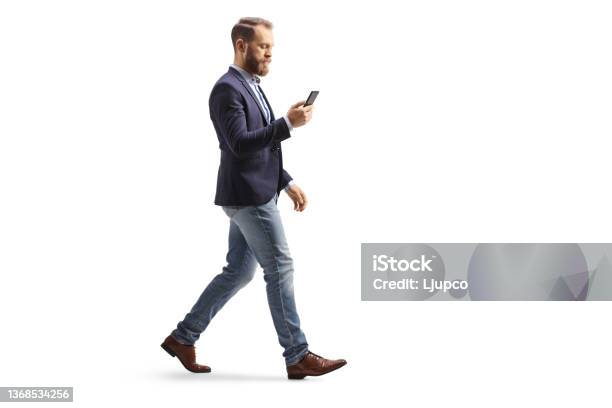 Full Length Profile Shot Of A Man In Suit And Jeans Using A Mobile Phone And Walking Stock Photo - Download Image Now