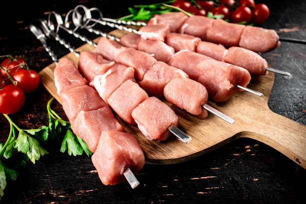 istock Pork kebab raw on a cutting board with tomatoes and herbs. 1368534352