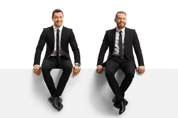 istock Two young professional men in suits sitting on a panel and looking at camera 1368534551