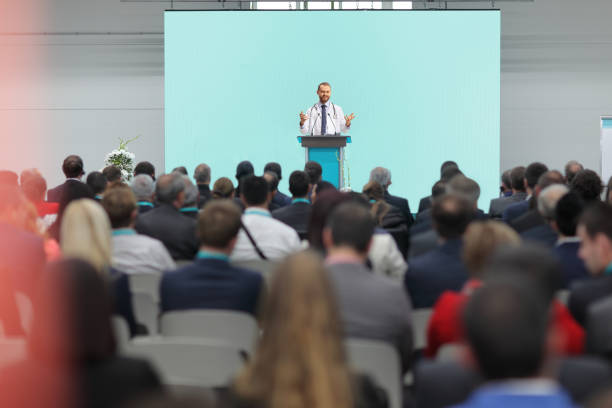 Male doctor giving a speech on a podium at a conference Male doctor giving a speech on a podium at a conference in front of an audience business conference photos stock pictures, royalty-free photos & images